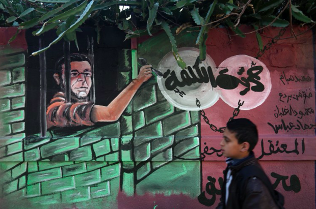 A Palestinian boy walks past a mural depicting Palestinian journalist Mohammed al-Qiq, during a demonstration on 1 February, 2016 in Gaza city (AFP) 