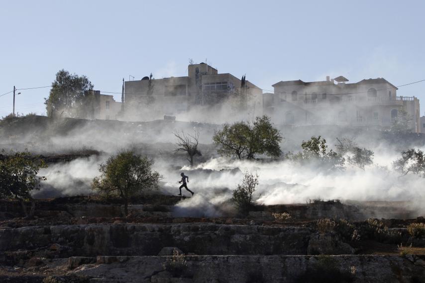 A Palestinian runs after Israeli security forces fired tear gas during clashes against Israel's military operation in Gaza, outside Ofer prison near the West Bank city of Ramallah, November 15, 2012. G4S, which supplies security technologies to the prison, is selling its business in Israel in what it says is a purely commercial decision.